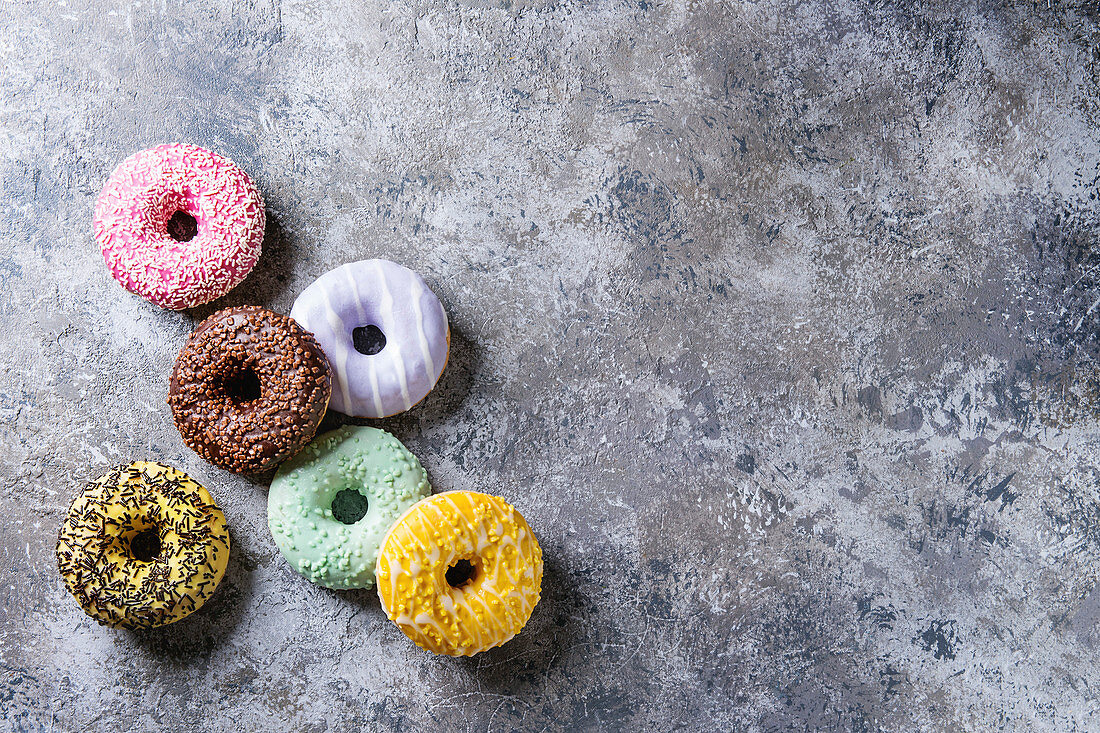 Sechs verschiedene bunt glasierte Donuts auf grauem Untergrund