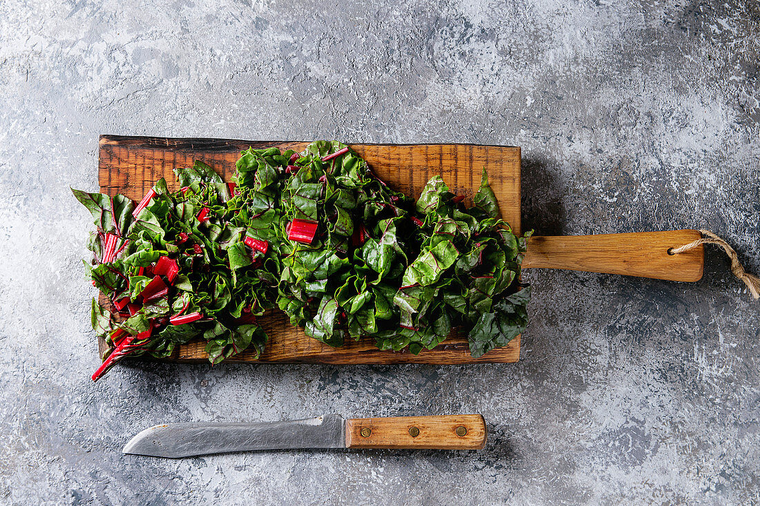Cutting fresh chard mangold salad on wooden chopping board with knife over gray texture background