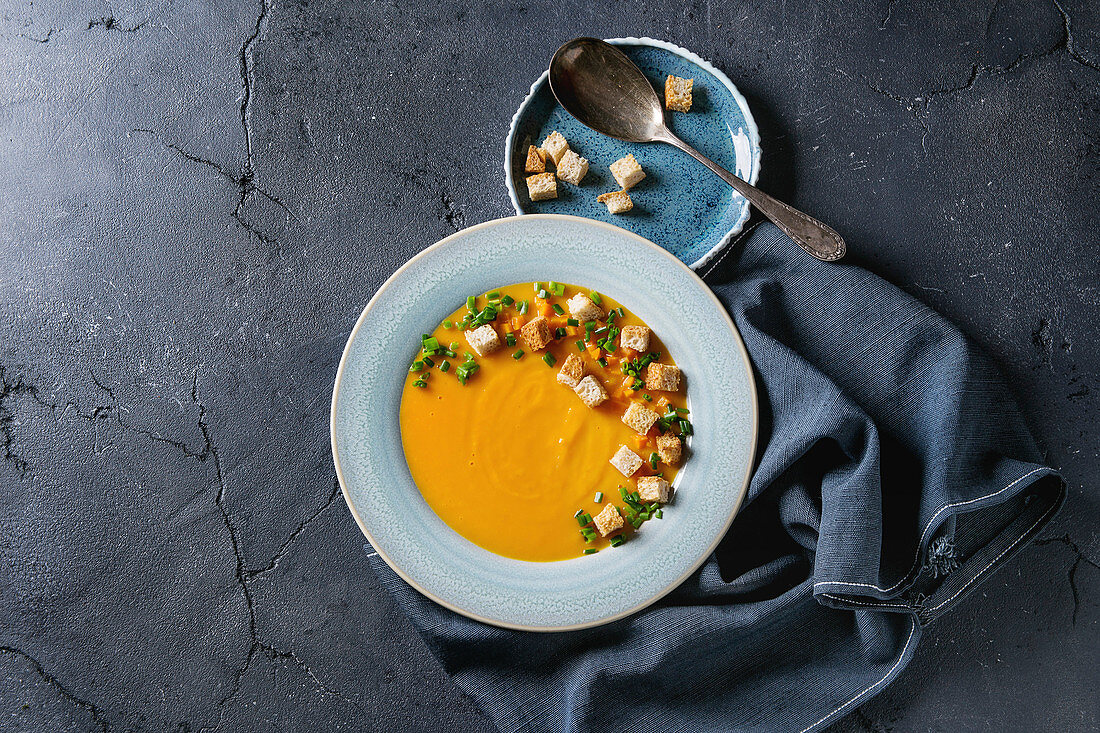 Plate of vegetarian pumpkin carrot soup served with croutons and onion on textile napkin