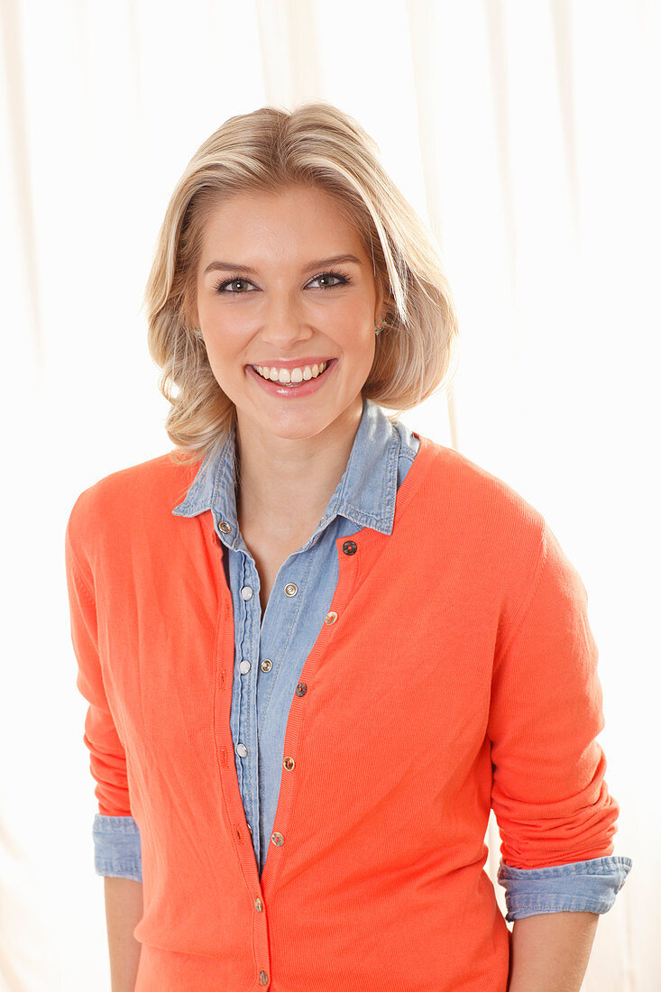 A young blonde woman wearing a denim shirt and an orange cardigan