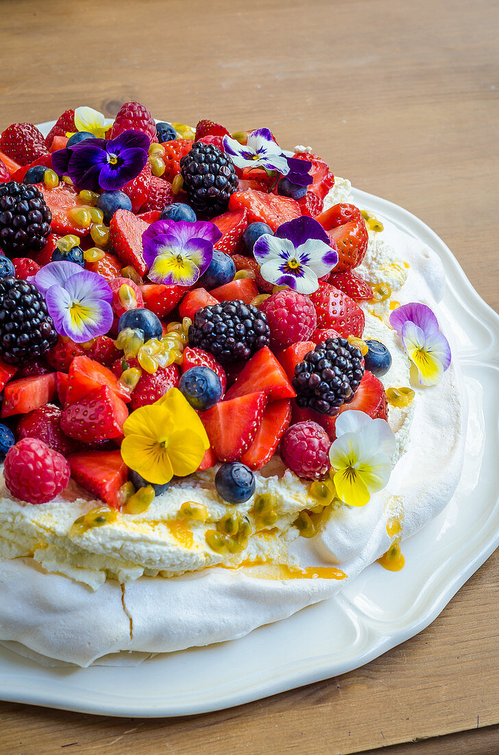 Pavlova with whipped cream, berries, passion fruit and edible flowers