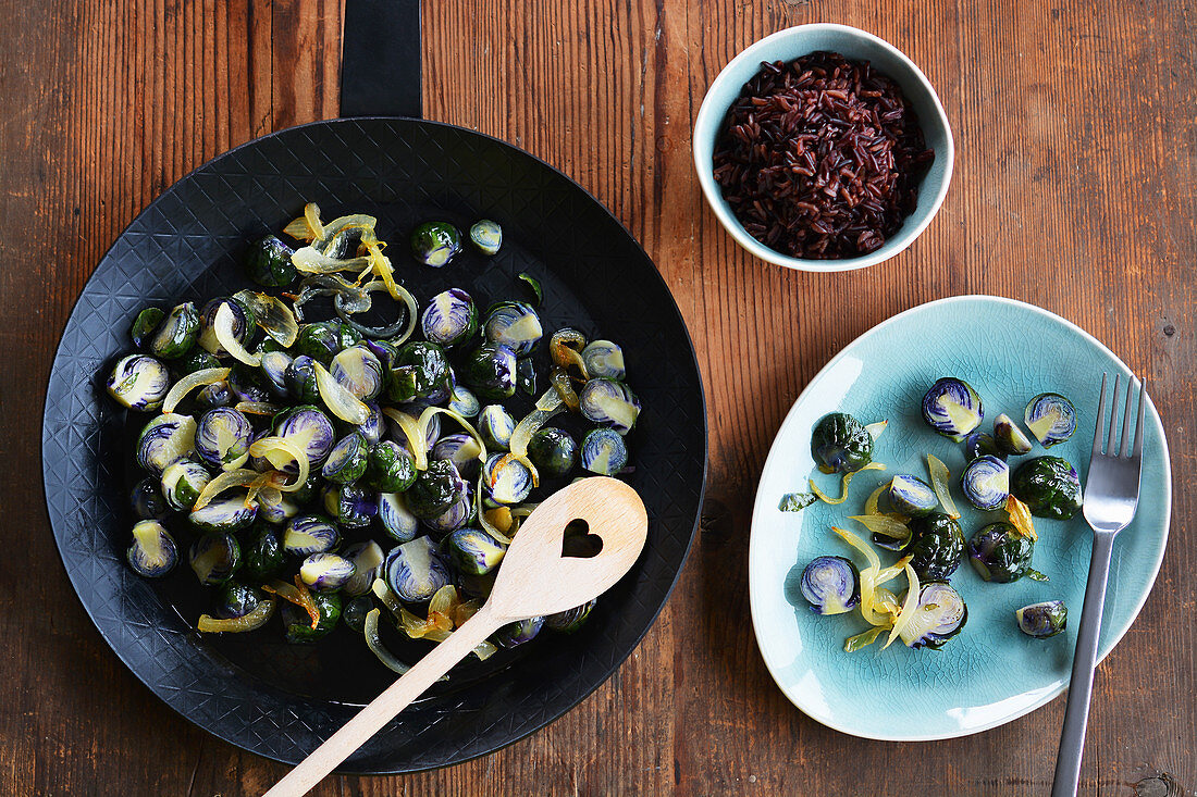 Fried Brussels sprouts in a pan and on a plate next to a bowl of wild rice