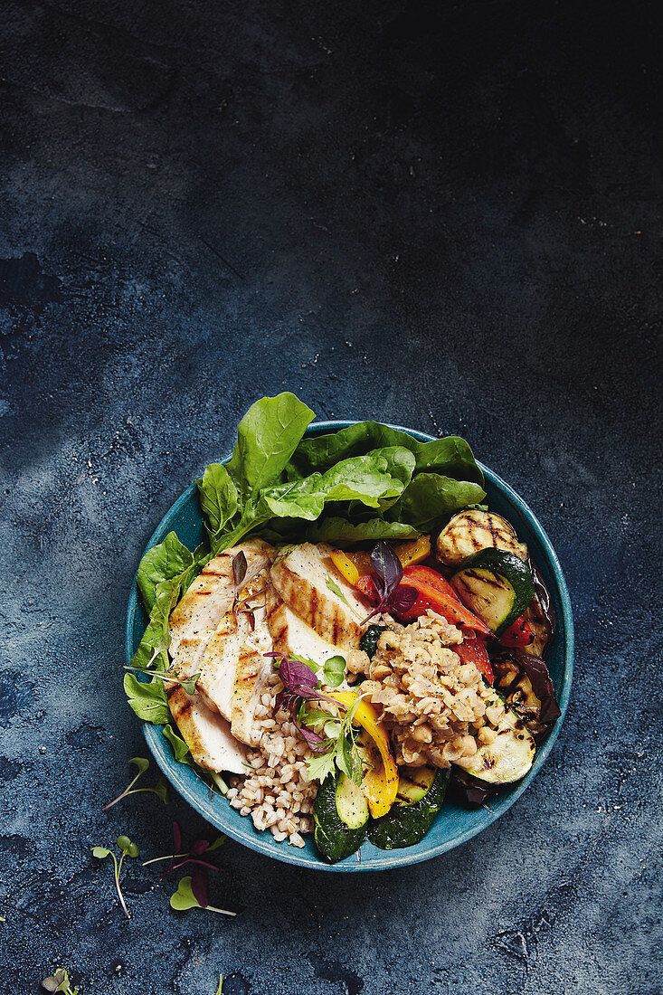 A salad bowl with grilled chicken breast, vegetables and barley