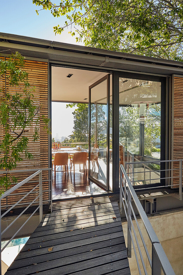 Steg zum modernen Architektenhaus mit offener Glastür zum Esszimmer