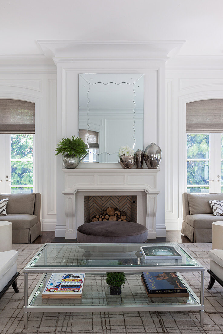 Glass coffee table and brown ottoman in front of white fireplace with mirror