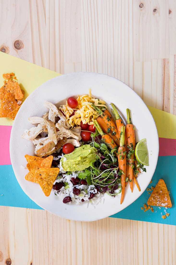 A burrito bowl with chicken, vegetables, rice, cheese and taco crisps