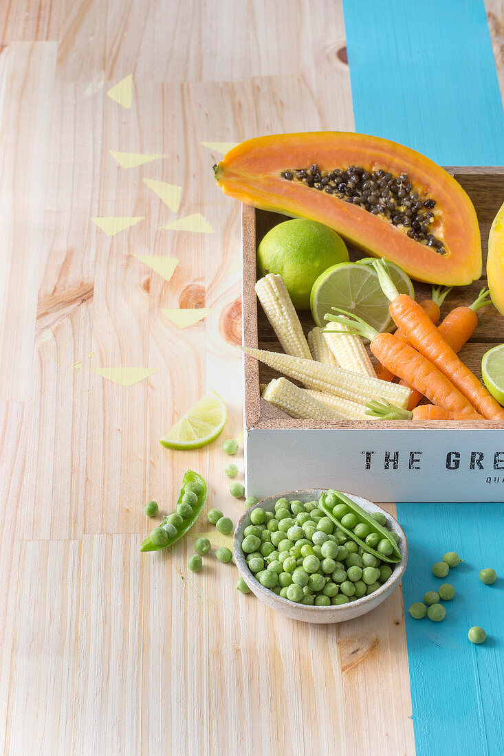 Fresh fruit and vegetables in a wooden box behind a bowl with peas