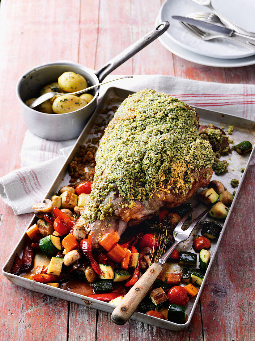 A leg of lamb with a herb crust, herb potatoes and oven-roasted vegetables