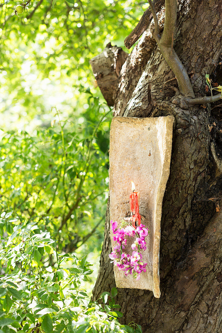 Alter Dachziegel als Kerzenleuchter mit Kränzchen aus Wicken am Apfelbaum im Garten