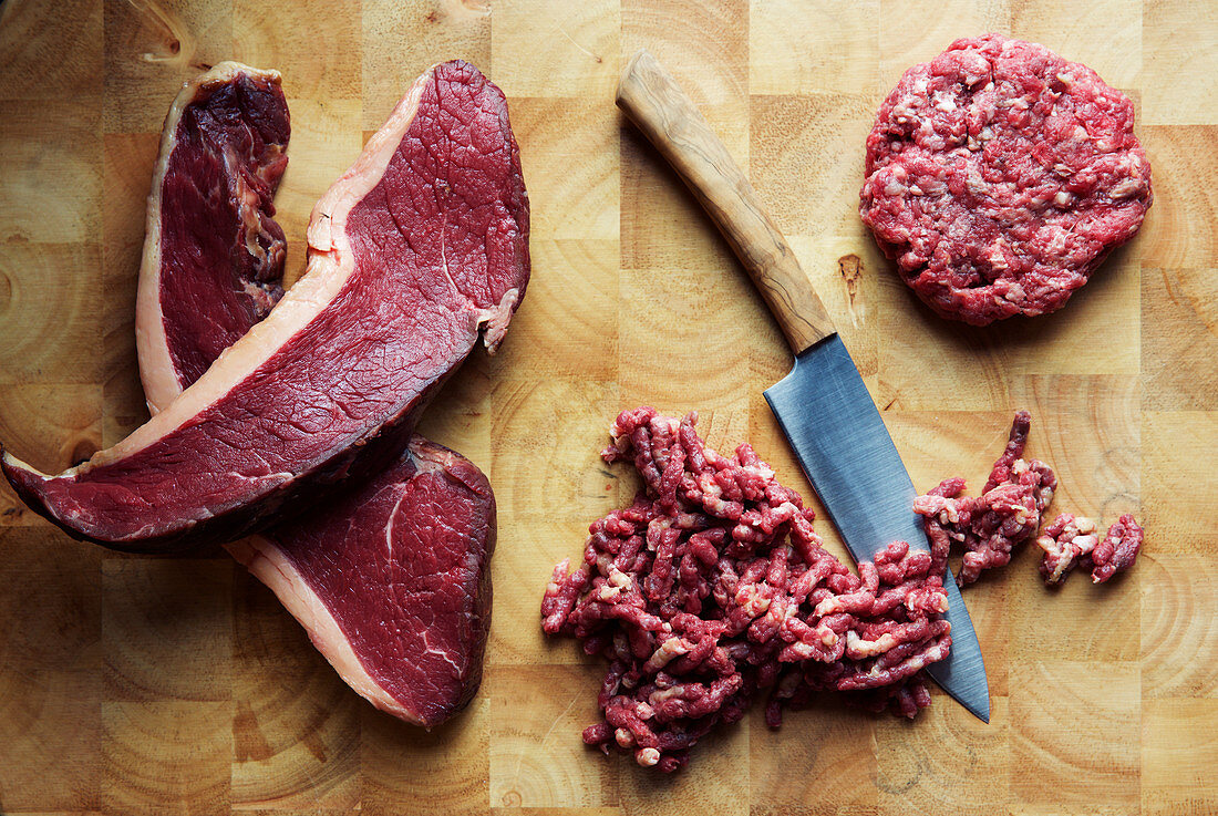 Beef steaks, minced meat and a beef patty with a knife on a chopping board
