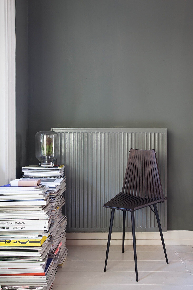 Schwarzer Stuhl und Zeitschriftenstapel vor Heizkörper an dunkler Wand