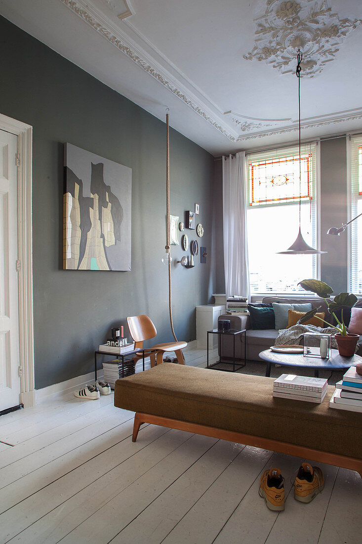 Books on retro couch, dark wall and white wooden floor in living room of period apartment