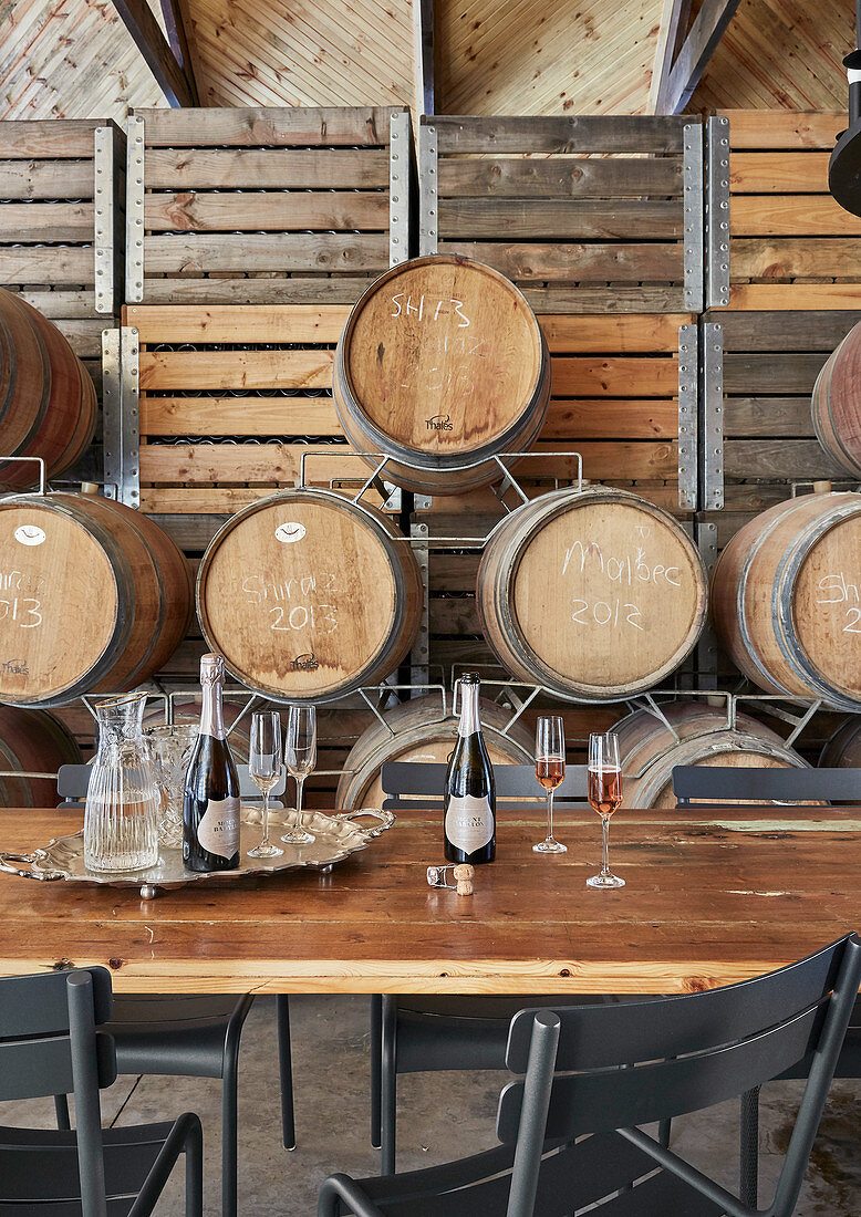 Champagner auf Holztisch vor rustikalen Weinkisten und Holzfässern