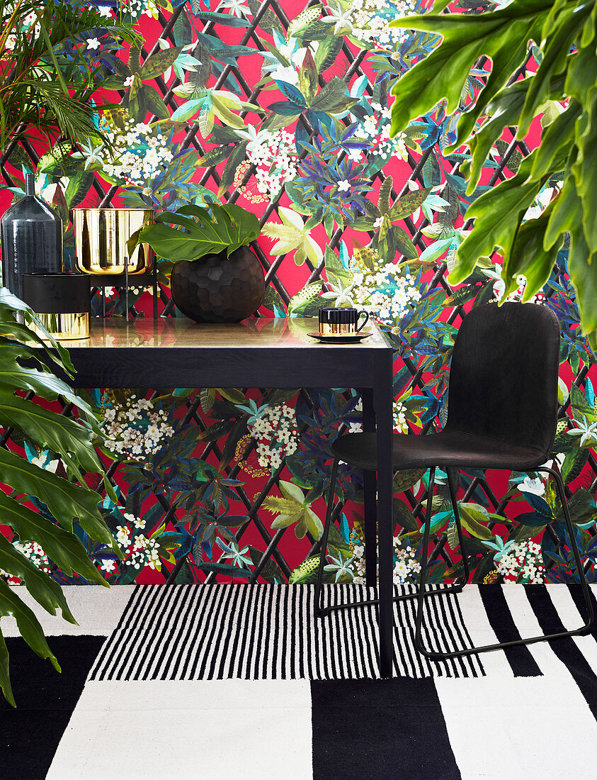 Black and gilt table in front of colourful leaf-patterned wallpaper