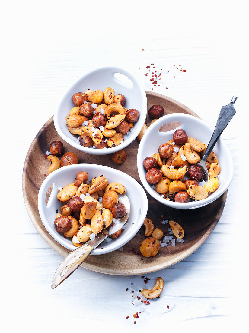 Spicy roast nuts in small bowls on a wooden plate