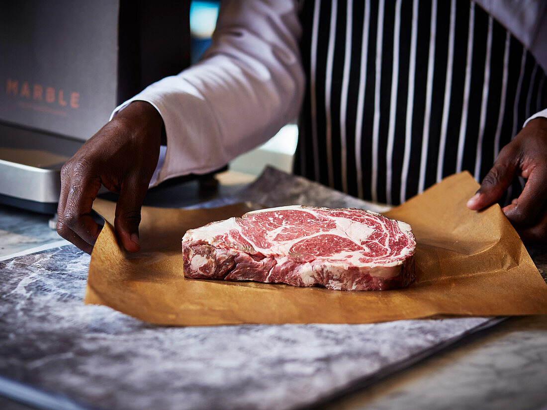 A man holding a raw ribeye steak on butchers paper