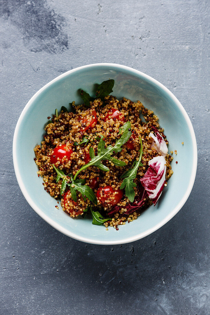 Salad with quinoa, tomato and arugula in bowl on concrete background