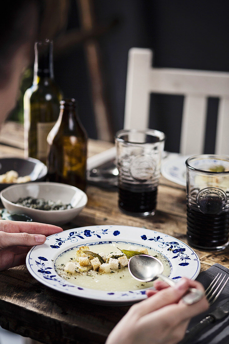 Woman eating a cauliflower soup on a wooden dining table