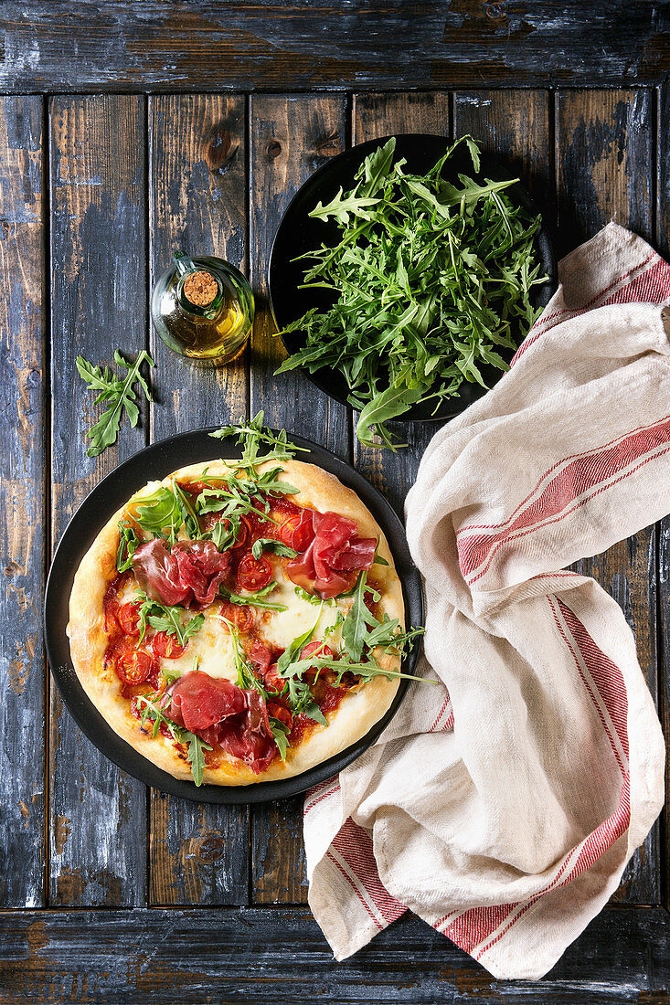 Selbstgemachte Pizza mit Tomaten, Bresaola und Rucola (Aufsicht)