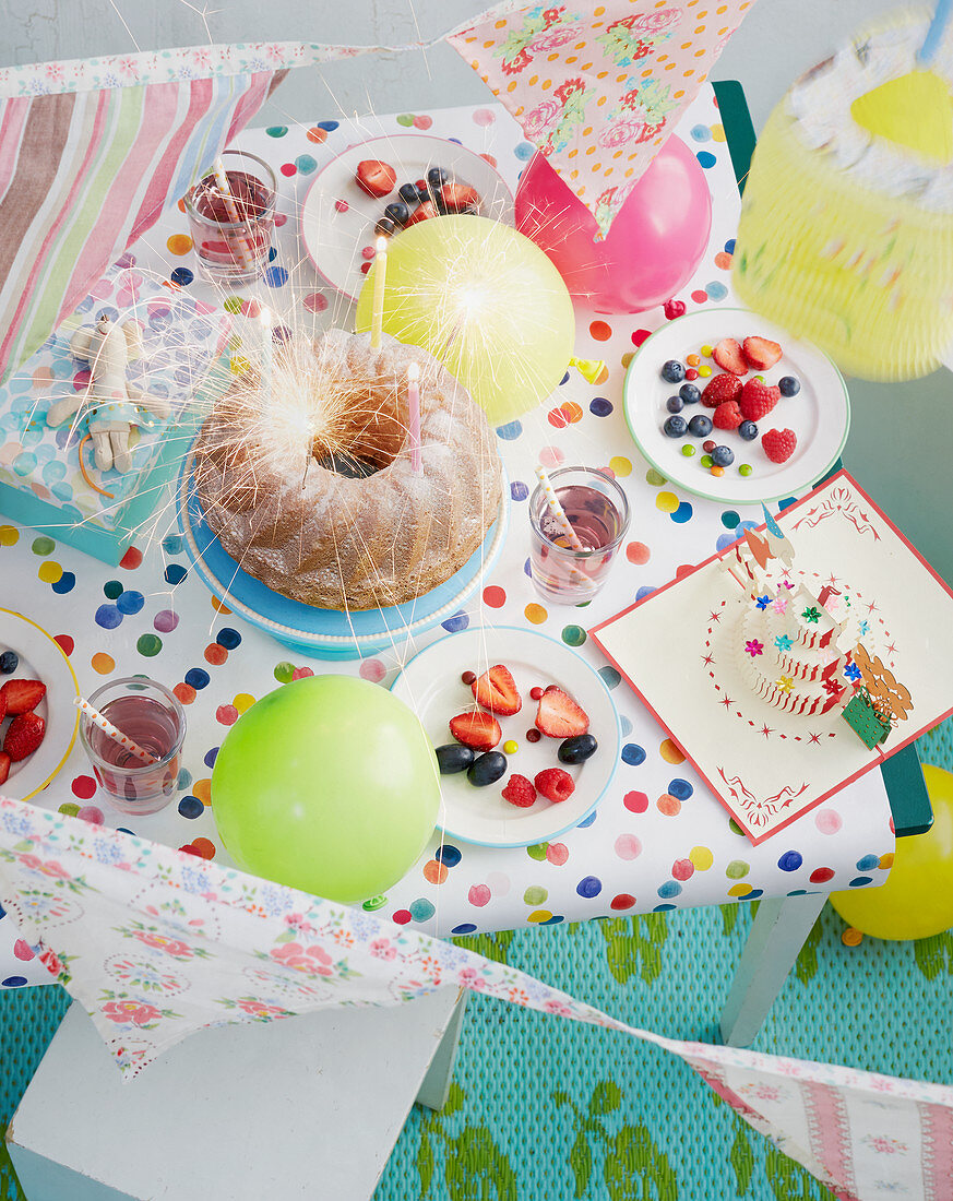 A table laid for a child's birthday part with cake, fruit and drinks