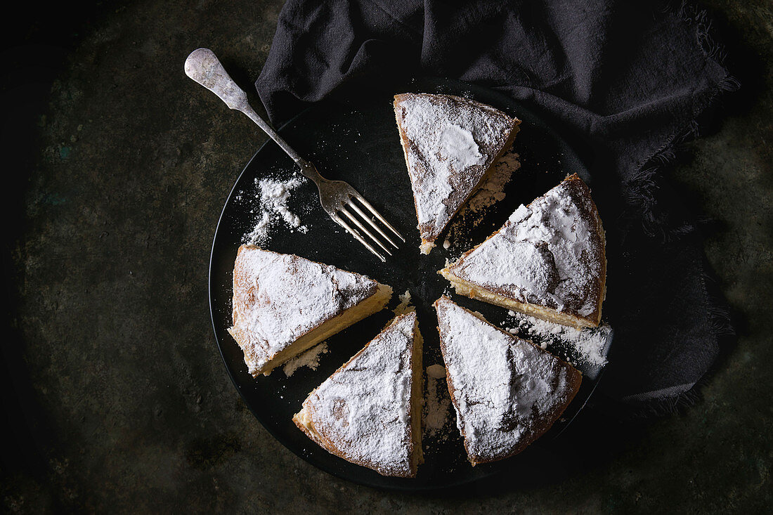 Torte mit Custard Cream und Puderzucker, geschnitten vor schwarzem Hintergrund