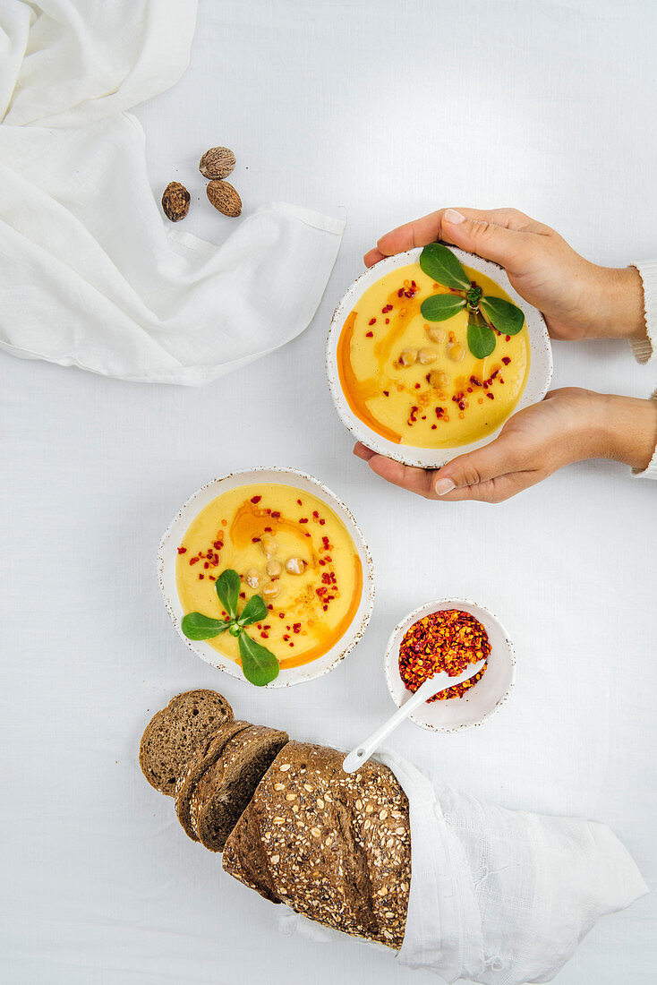 Vegane Kürbiscremesuppe im Schälchen mit Chiliflocken, Portulak und Brot