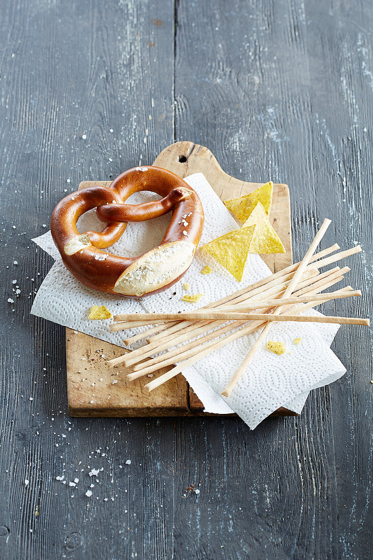 A pretzel, grissini and tacos on a chopping board