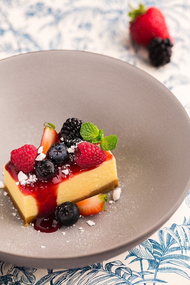 A slice of cheesecake with fruit sauce and fresh berries