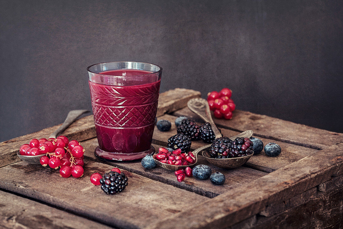 Saftglas und rote Johannisbeeren, Granatapfelkerne, Blaubeeren und Brombeeren auf Holzkiste