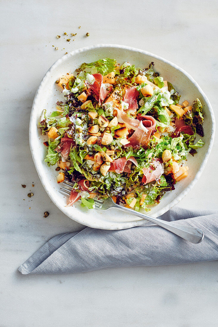 A colourful mixed leaf salad with melons, ham and macadamia nuts