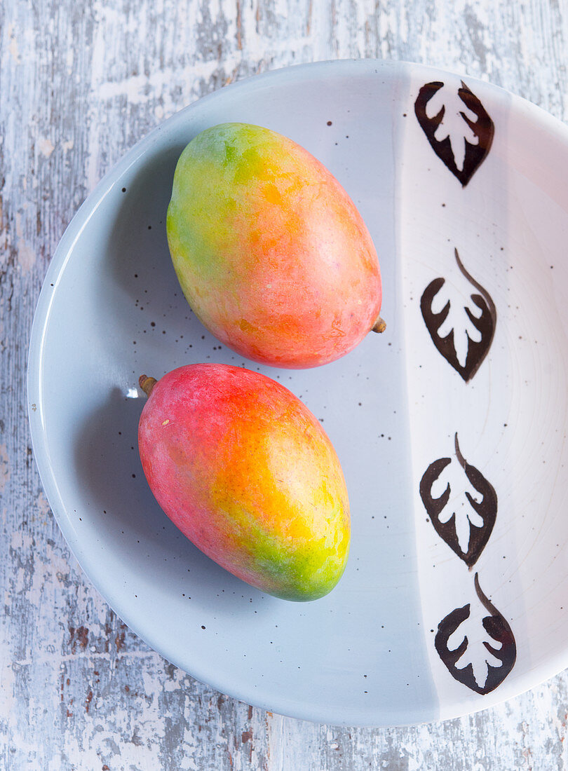 Two whole mangos on a ceramic plate