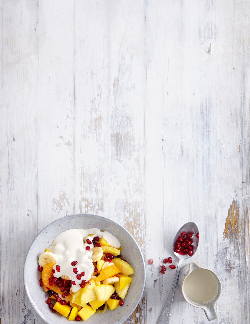 Yellow fruit salad with yoghurt sauce and pomegranate seeds