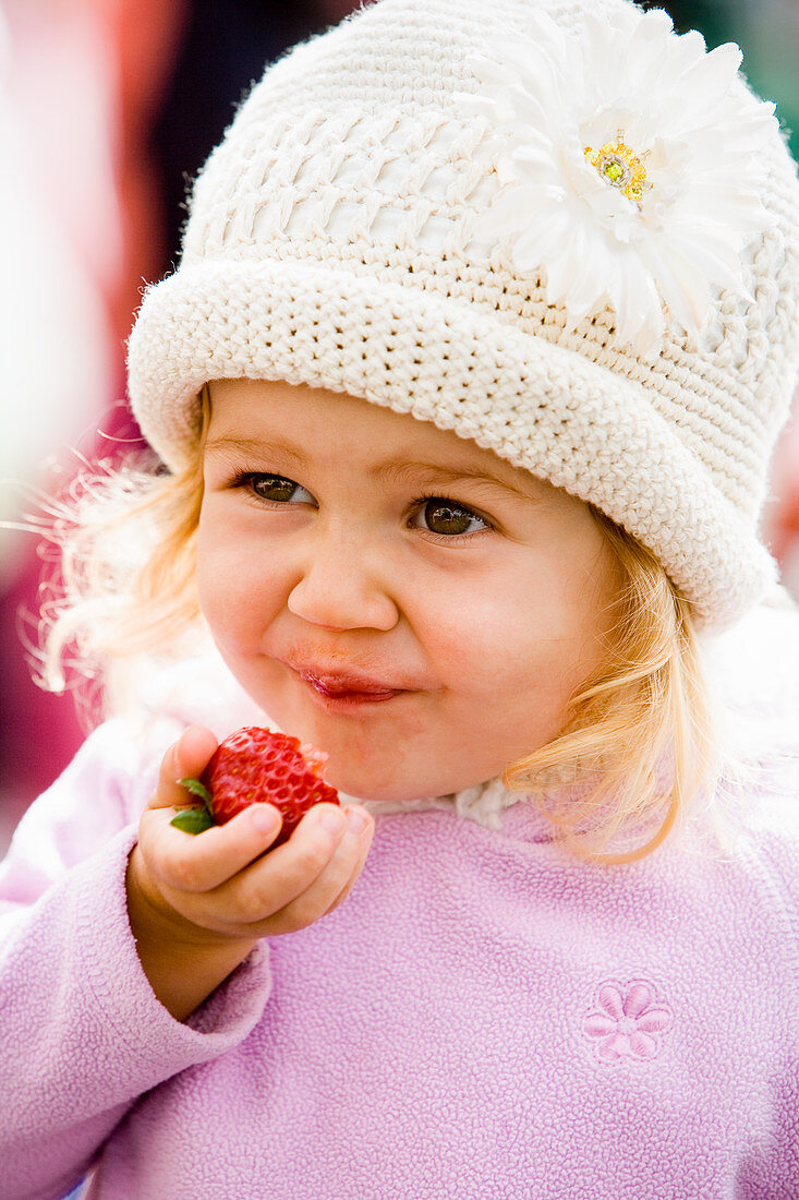 Kleines Mädchen isst frische Erdbeere auf einem Markt
