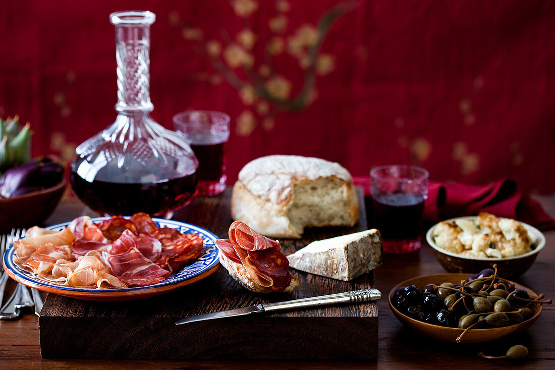 Schinkenplatte mit Oliven, Blumenkohlsalat, Käse, Brot, Artischocken und Wein
