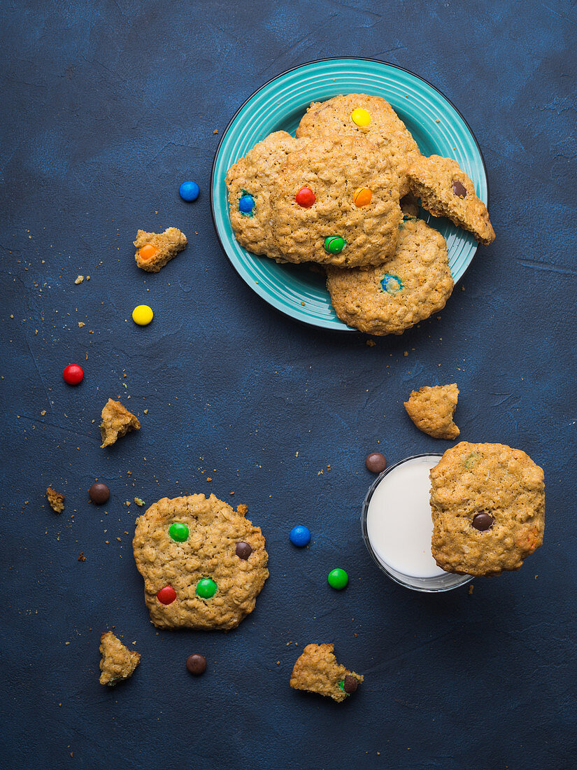 Oatmeal butter cookies with colorful candies with a glass of milk on blue background