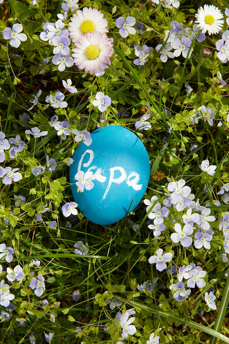 Blue Easter egg painted with chalkboard paint and labelled 'Papa' lying on spring lawn
