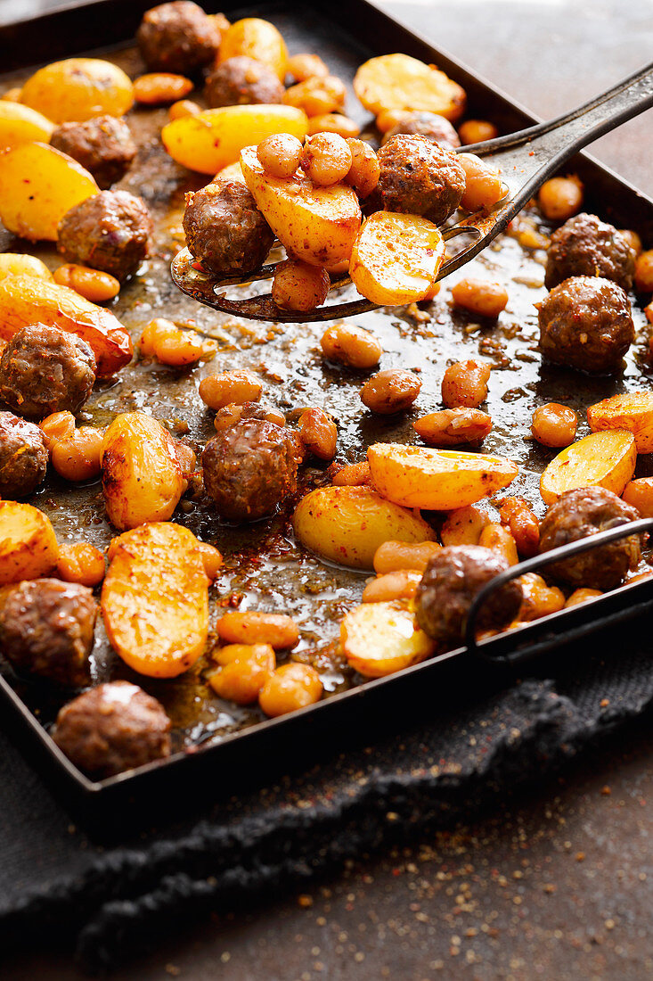 Warm beans and potatoes with meatballs on a baking tray