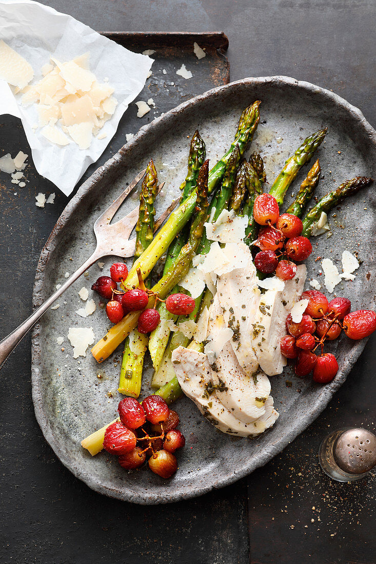 Asparagus with chicken breast and grapes on a baking tray
