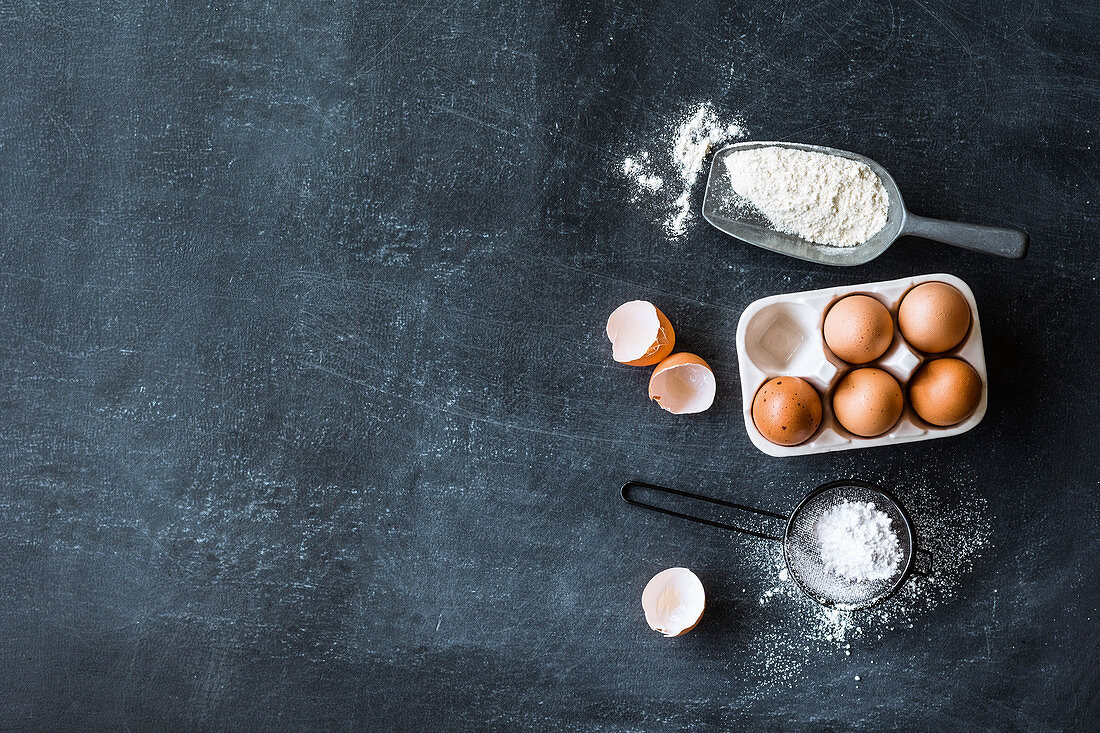 Eggs, flour and icing sugar on a grey surface