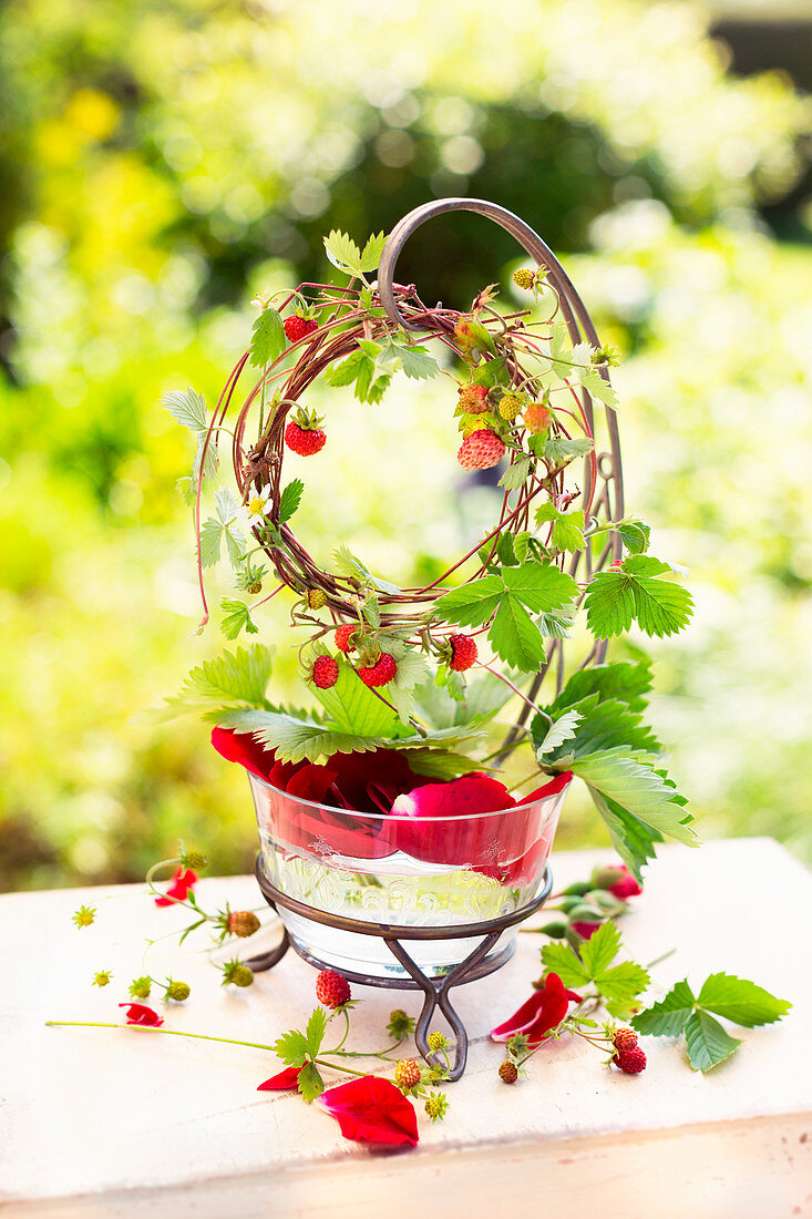 Kränzchen aus Trieben von Walderdbeeren auf Glassschale mit Wasser und Rosenblättern