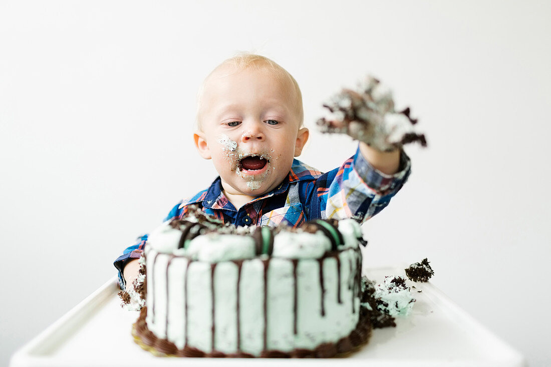 A little boy sitting in a high chair and eating a birthday cake
