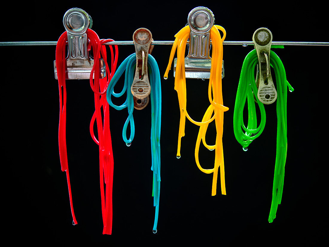 Different coloured spaghetti hung fom clips in front of a black background