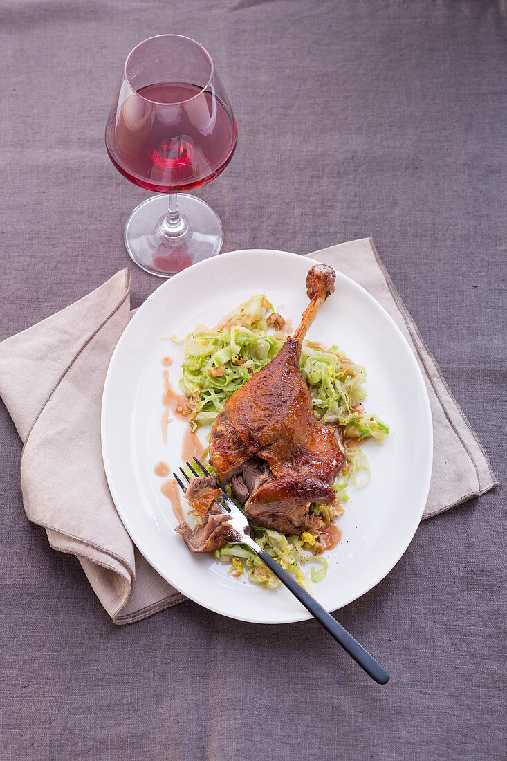 A goose leg with spicy cabbage served with red wine