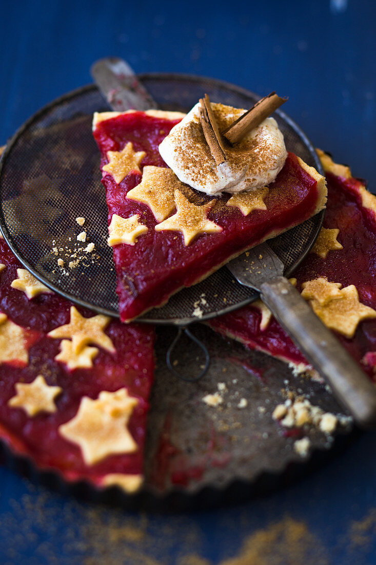 A slice of plum tart decorated with pastry stars, cream and cinnamon