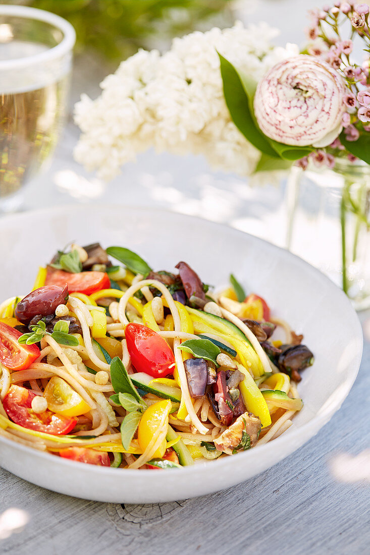 Spaghetti mit Tomaten und Oliven auf sommerlichem Tisch im Freien