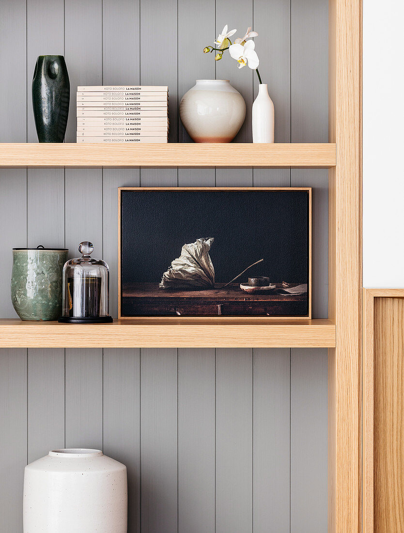 Decorative objects, flower vase and books on an open wooden shelf