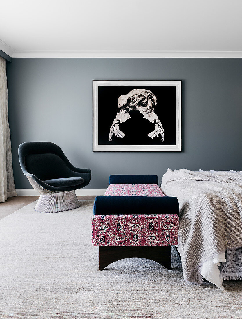 Polstersessel, Tagesbett am Bettende und grossformatige Fotografie an grauer Wand im Schlafzimmer