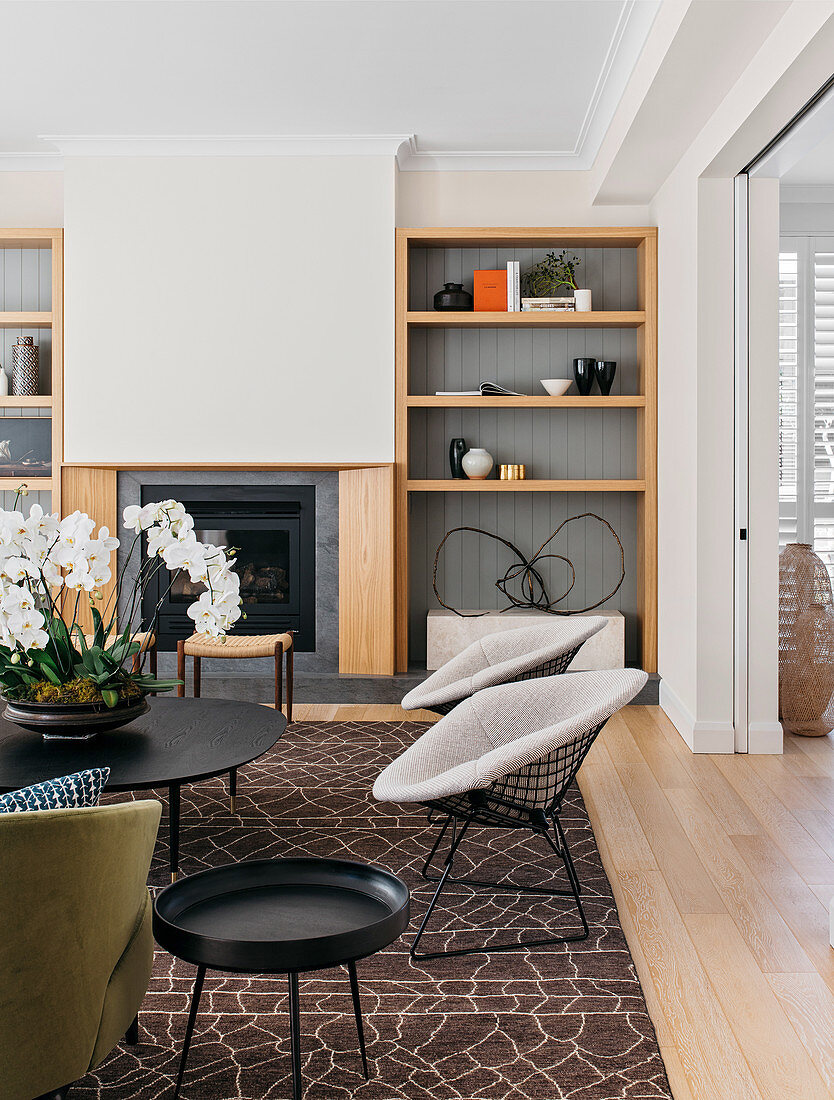 Classic chairs and coffee table with orchid in front of built-in fireplace and open wooden shelf