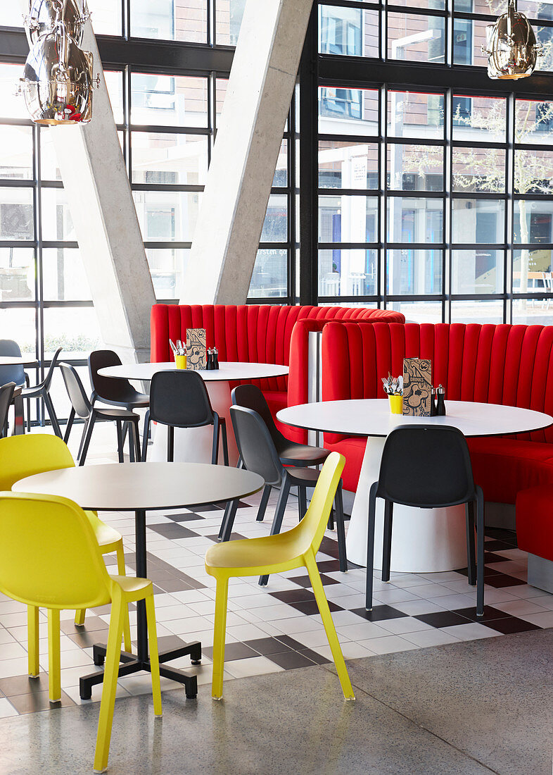 Round tables with yellow and white chairs in restaurant with glass façade