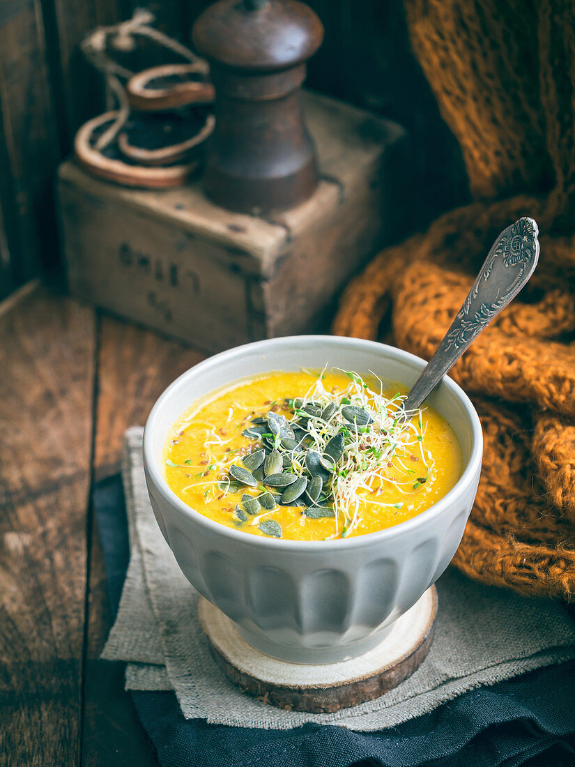 Creamy carrot soup served with sprouts and pumpkin seeds on a rustic background